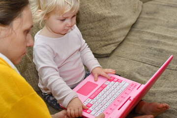 Fototapeta na wymiar Mom teaches the child to play on the children's toy laptop.