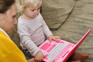 Mom teaches the child to play on the children's toy laptop.