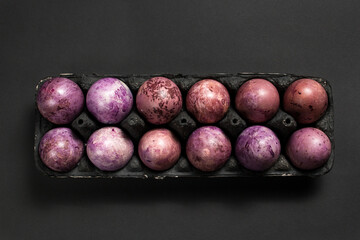 Colorful painted eggs in a black egg box on the black background. Easter flat lay with copy space