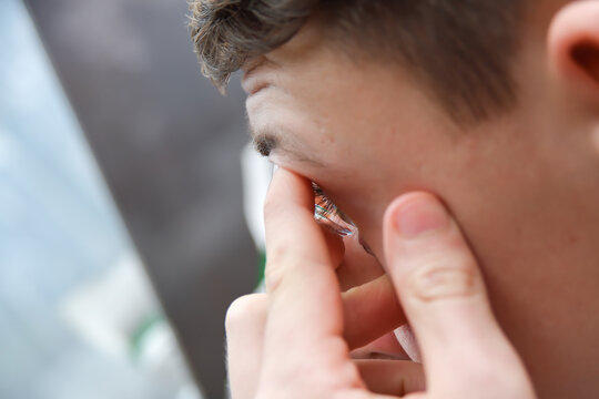 A teenager puts on a contact lens over his eye. Macro photo of a medical theme.