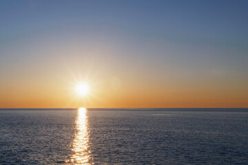 The setting sun goes into the sea on the horizon with a light track and reflections on the sea.