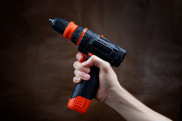 The male hand holds an electric screwdriver on a dark brown background.