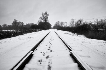 Footprints in the snow on old railroad track in winter, black and white.