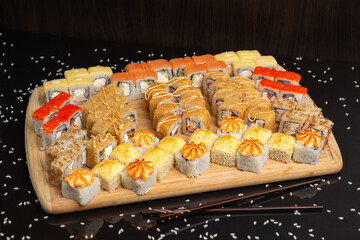 Big sushi set on light wooden dish isolated on black background