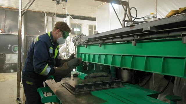 A worker in a plastic recycling factory begins the process of creating a trash can. Pours a special mixture into the oven, forms the mass on the press, takes out the finished product.