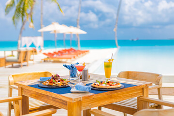 Luxury resort hotel poolside, outdoor restaurant on the beach, ocean and sky, tropical island cafe, tables, food. Summer vacation or holiday, family travel. Palm trees, infinity pool, cocktails, relax