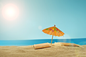 Beach umbrellas and sunbeds on the sand. Stylized cardboard beach. Paper umbrellas for cocktails in the background. The concept of rest, sea and vacation. Artificial wooden deck chairs.