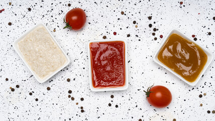 Three kinds of sauces on a white cement background: traditional classic ketchup, white sauce, sweet and sour Chinese sauce. Top view copy space