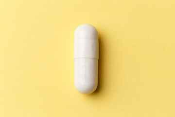 Pharmaceutical medicine pills, tablets and capsules on colourful yellow background. Top view. Flat lay. Copy space. Medicine concepts. Minimalistic abstract concept. White medicine capsule