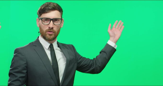 Young professional TV presenter in suit and glasses conducts live news and completing block gets up from background of chromakey