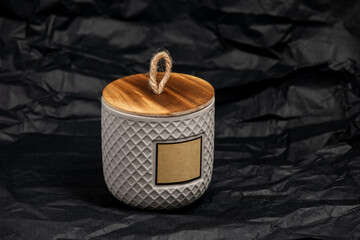 Label mockup of the ceramic jar with handmade candle on black paper background. Product package with blank label and bamboo wooden cap.