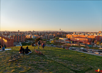 Several people watching Madrid's skyline from a grassy hill at susnet. 