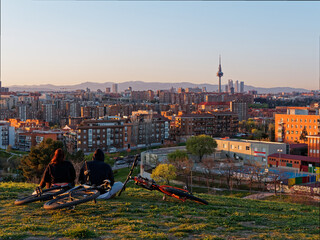 Dos personas con sus bicicletas sentadas en el césped mirando la ciudad de Madrid al atardecer