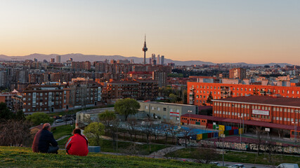 Sunset virew of the city of Madrid. Two persons sitting on the grass while looking at the skyline