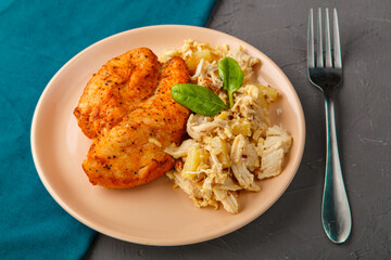 Baked chicken breast with salad on a plate decorated with spinach next to a fork on a concrete background on a blue napkin stand.