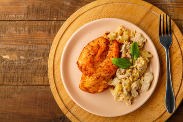 Baked chicken breast in sauce with salad on a plate next to a fork on a wooden table on a round stand.