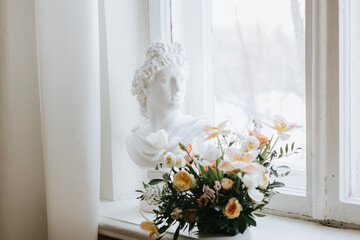 A statue of a bust of a woman stands on the window next to a bouquet of flowers, a concept of spring and International Women's Day