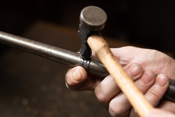 foreground, hammer hammering a silver ring to shape it in a jewelry workshop.