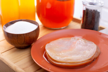 Set for preparing homemade fermeted drink. Glass gar with komucha, bottle with ready beverage, black tea brew, bowl of sugar and plate with scoby. Selective focus