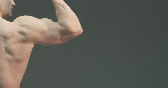 Muscular male hand. Athletic guy showing biceps on gray studio background with copy space. Close up 4K video.