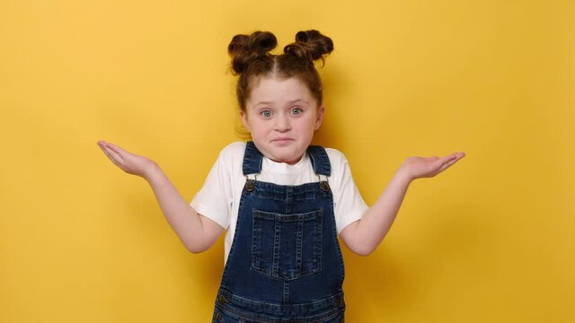 Confused little girl shrug as sign of doubt making choice. Headshot of surprised, frustrated small kid looking at camera hold palms up isolated on yellow studio background. People emotion concept