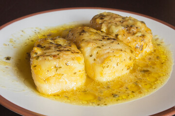 Presentation of three tasty hake loins in green sauce on a white plate. Fish and healthy food.