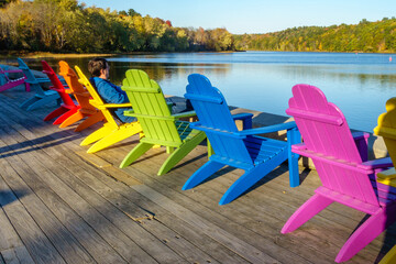 Man relaxing in a row of brightly colored adirondack chairs along waterfront in fall