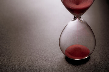 Sand passes through an hourglass, measuring the travel time counting down to the deadline, against a dark background with space for text © Nana_studio