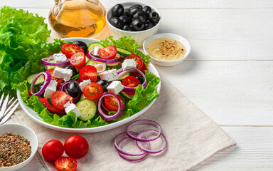 Greek salad and fresh ingredients on a white wooden background.