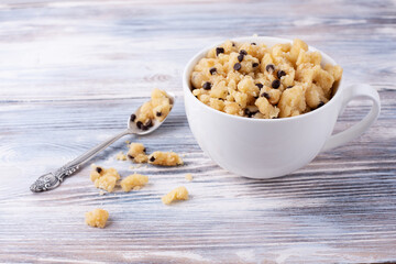 Bowl and spoon with edible cookie dough and crumbs on the white wooden background.