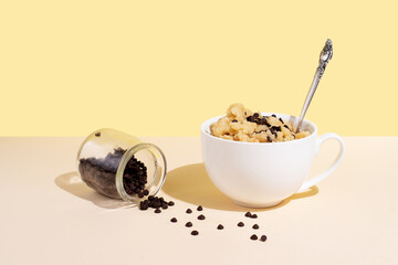 Edible cookie dough in white cup with chocolate chips and spoon on a yellow background in sunlight.