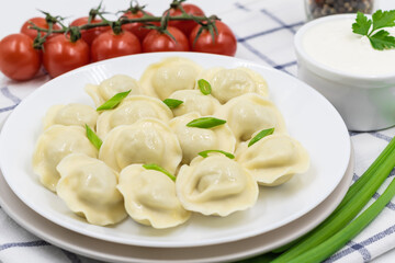 Boiled Russian dumplings on a plate. Served with sour cream, green onions and cherry tomatoes on a checkered napkin.