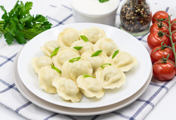 Boiled Russian dumplings on a plate. Served with sour cream, green onions and cherry tomatoes on a checkered napkin.