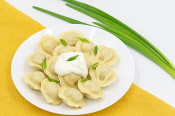Boiled Russian dumplings with sour cream and green onion on a plate on a yellow napkin. Top view.