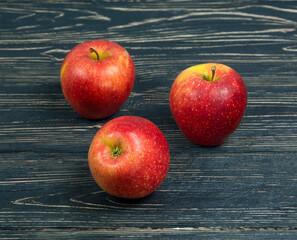 Three red apples on a dark wooden background.