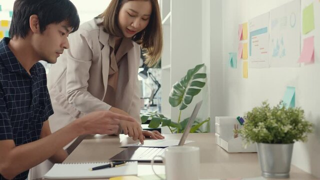 Group of young asia creative businessman and businesswoman team discuss project compare point in paperwork and laptop on table working and communicating together sitting on office desk at workplace.