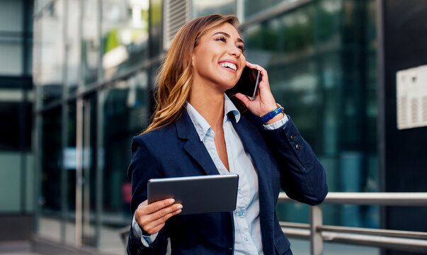 Businesswoman holding tablet and making a phone call in front of the corporation. Business, lifestyle concept