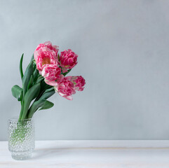 Pink tulips in a glass vase stand on the table, on a gray background, copy space.