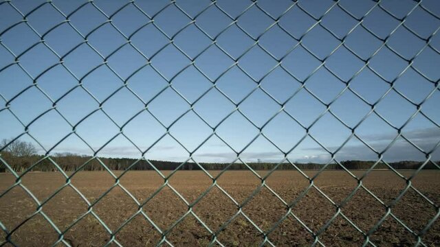 Licht und Schatten im Zeitraffer mit Maschendrahtzaun im Vordergrund