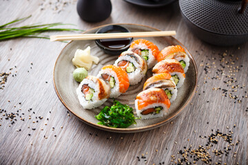 Sushi maki rolls with salmon, eel, avocado, cucumber on a plate with chopsticks, soy sauce, wasabi and ginger. Japanese traditional fish food closeup served for lunch in modern gourmet restaurant