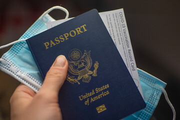 Passport of USA with COVID-19 Vaccination record card and medical mask in hand. Close up view. Travel during pandemic time concept. - obrazy, fototapety, plakaty