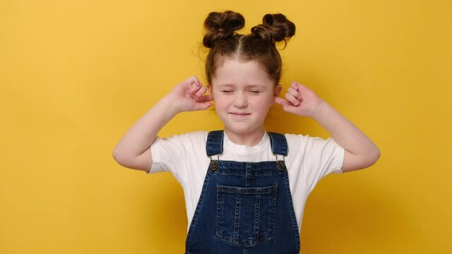 Portrait of annoyed little preschool girl close plug ears scream loudly tired by noisy sound, furious small child, avoid ignore unbearably loud noise ask quiet, isolated on yellow studio background