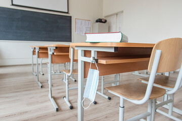 Book with a disposable protective mask on school table. Back to school  after pandemic