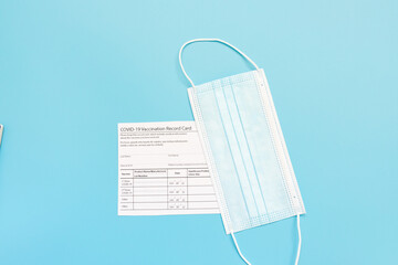 Vaccination record card, passport, a vial with covid-19 vaccine. syringe and mask on a blue...