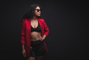 Una hermosa mujer de color, con una chaqueta sport color rojo en un fondo negro con gafas de sol