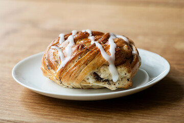 Freshly baked cinnamon roll (also cinnamon bun or cinnamon swirl) with icing on white plate on wooden table.