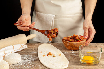 A Turkish woman is preparing kiymali pide, traditional flatbread with ground meat paste onto flattened dough and egg is spread on top of the mixture before baking in brick oven.