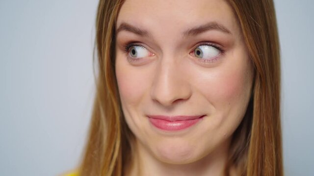 Closeup surprised woman smiling at camera on grey background. Funny girl face 