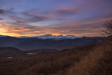Naklejka na ściany i meble Morning landscape in the mountains of Adygea. View of the valley and snowy peaks against a background of blue sky and pink clouds. The sun rises behind the Caucasus mountains