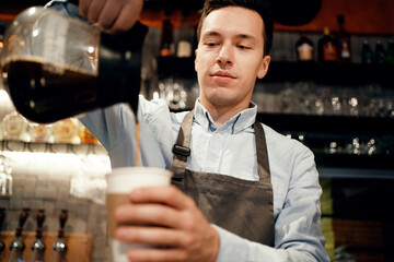 Clothing apron uniform of the bar staff. A male barista makes a takeaway coffee. Works in his small business restaurant cafe. Copy space. Modern interior.